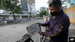 Un conductor de mototaxi coloca un cartel de precio que dice "mínimo un dólar" en Caracas, Venezuela. Junio 1, 2020.