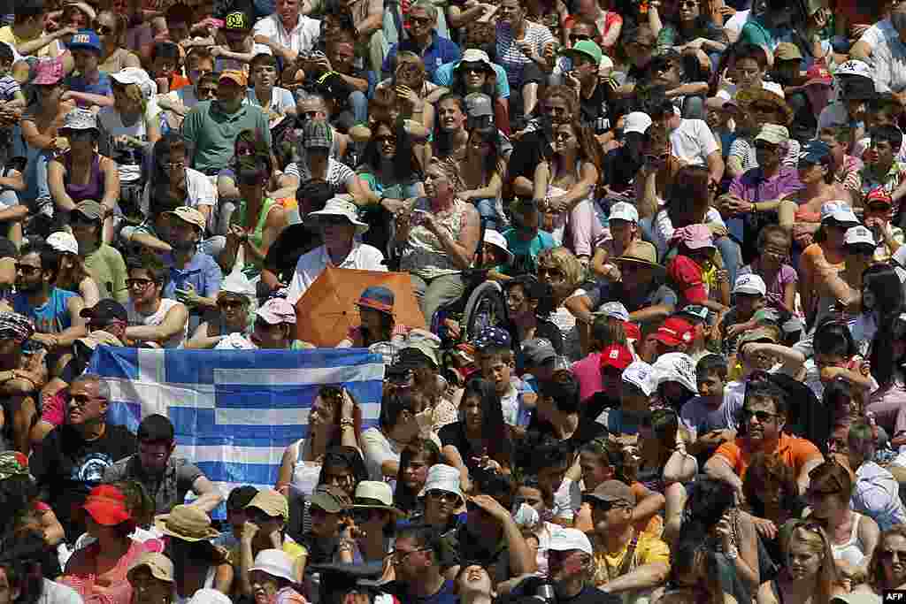 Spectators hold a Greek national flag, during the lighting of the Olympic flame ceremony on Thursday. May 10, 2012, in Ancient Olympia, Greece. The flame will be carried from the birthplace of the Ancient Olympics to London, where the 2012 Summer Game