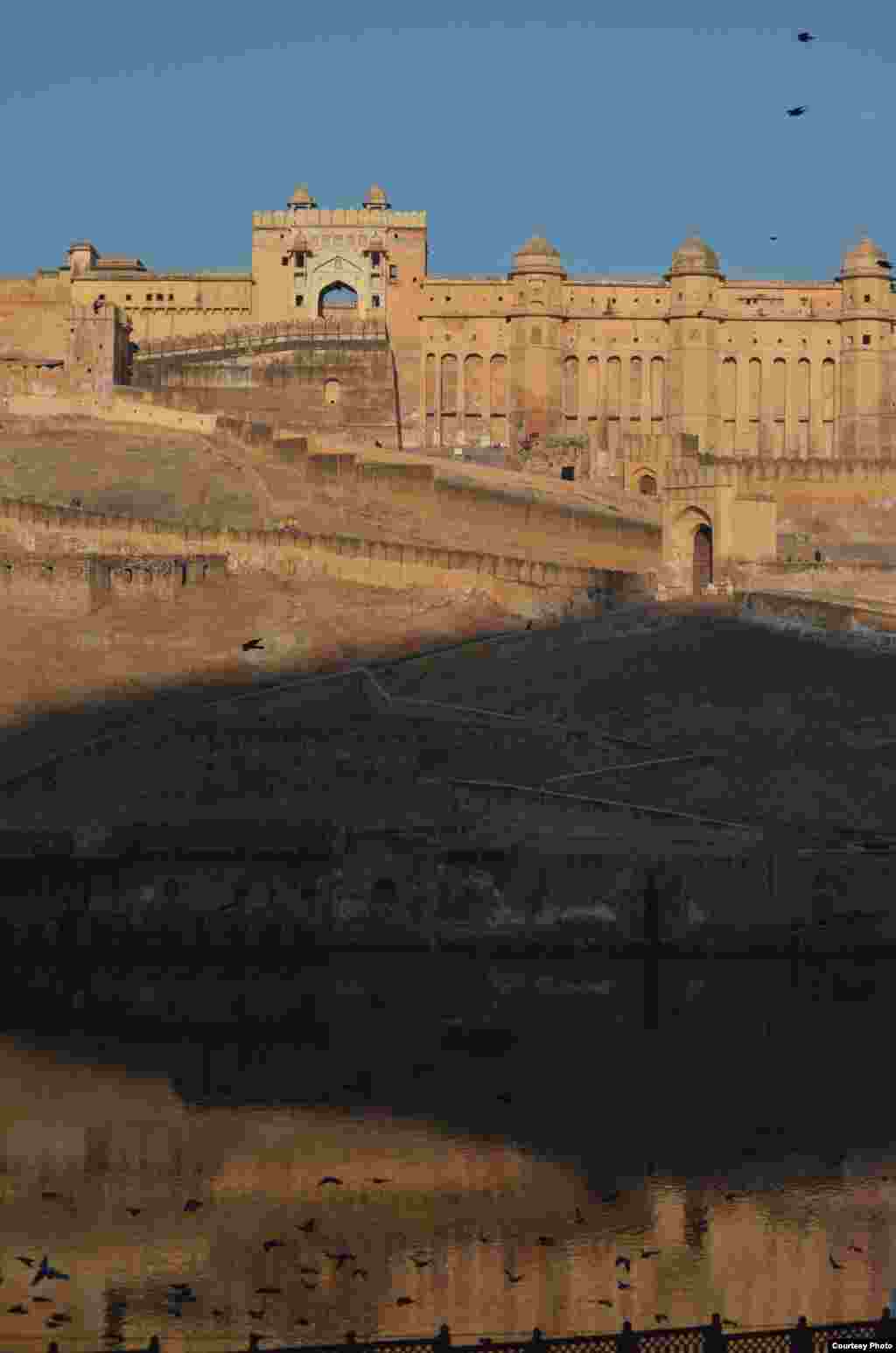 C&ocirc;ng tr&igrave;nh Amber fort_Jaipur_India trong nắng sớm, khi b&oacute;ng đổ tuyệt đẹp của d&atilde;y n&uacute;i v&agrave; đ&agrave;n chim ph&iacute;a trước đổ l&ecirc;n mặt dựng v&agrave; mặt nước của ph&aacute;o đ&agrave;i h&ugrave;ng vĩ với cảnh quan đồi (Ảnh: Tran Phuong Mai)