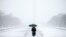The Washington Monument and the Reflecting Pool are visible behind Claudia Marusanici as she makes her way towards the Lincoln Memorial on the National Mall, March 5, 2015, in the falling snow.
