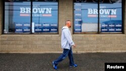 FILE - A pedestrian walks past U.S. election campaign posters in Manchester, New Hampshire.