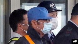 Un hombre cubierto con una máscara facial, que se cree que es el expresidente de Nissan Carlos Ghosn (centro, con gorra azul), sale del Centro de Detención de Tokio, en Tokio, el 6 de marzo de 2019 tras depositar una fianza.