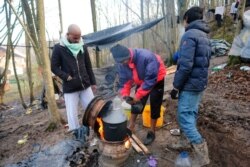 Migrants cook on a stove improvised from wheel rims at a makeshift camp in a forest outside Velika Kladusa, Bosnia, Jan. 5, 2021.