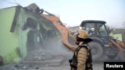 FILE - A police officer gestures as a bulldozer demolishes a property during a government demolition drive in Haldwani in the northern state of Uttarakhand, India, on Feb. 8, 2024.