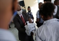 Principal Jean Marc Charles delivers face masks to pupils, to prevent the spread of the coronavirus disease, before attending to the first day of school after holidays, at Lycee National de Petion Ville, in Port au Prince, Aug. 10, 2020.