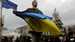 Seorang demonstran anti-pemerintah Yanukovych memegang bendera Ukraina di Lapangan Merdeka, Kyiv, Ukraina (25/2).