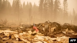 An American flag is placed on a burned fire engine at a burned fire station in downtown Greenville, California on August 7, 2021. - The Dixie Fire has now ravaged 446,723 acres in four counties, up from the previous day's 434,813. That area is…