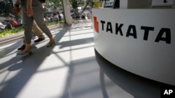 FILE - Visitors walk by a Takata Corp. desk at an automaker's showroom in Tokyo.