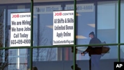 FILE - A woman walks past the signs of an employment agency, in Manchester, N.H., March 2, 2021.