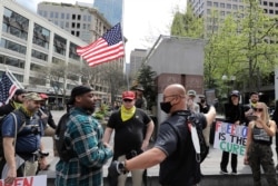 FILE - Members of a group wearing shirts with the logo of the far-right Proud Boys group argue with counterprotesters during a small protest against Washington state's stay-at-home orders, May 1, 2020, in downtown Seattle.