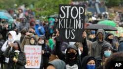 FILE - A protester holds up a sign that reads "Stop Killing Us," during a "Silent March" against racial inequality and police brutality, in Seattle, Washington, June 12, 2020.