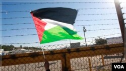 Seorang warga Tepi Barat mengibarkan bendera Palestina di pos pemeriksaan Beituniya (Foto: dok). Militer Israel dilaporkan menembak mati seorang remaja Palestina di dekat tembok pemisah Tepi Barat. 