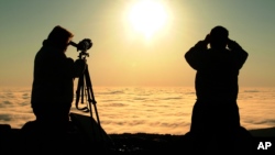 Dos personas observan a través de binoculares el tránsito de Venus frente al sol, en las montañas Cadillac, en el parque nacional Acadia, en Maine, Estados Unidos.