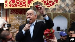 Israeli Prime Minister and head of the Likud party Benjamin Netanyahu holds a strawberry as he speaks during a visit to a market in Jerusalem, Feb. 28, 2020. 