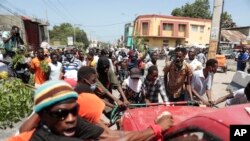 Para pengunjuk rasa mencoba membalikkan mobil untuk memblokir jalan selama protes terhadap ketidakamanan di Port-au-Prince, Haiti, Senin, 7 Agustus 2023. (AP/Odelyn Joseph)