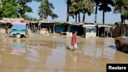 Seorang remaja Afghanistan berjalan di sepanjang jalan yang banjir di Sheikh Jalal, provinsi Baghlan, Afghanistan Minggu, 12 Mei 2024.