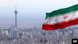 Iran's national flag waves as Milad telecommunications tower and buildings are seen in Tehran, Iran, Tuesday, March 31, 2020. In recent days, Iran which is battling the worst new coronavirus outbreak in the region, has ordered the closure of…