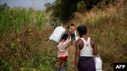 FILE - Myanmar refugees, who fled a surge in violence as the military cracks down on rebel groups, walk with food aid on the Thai border in Thailand's Mae Sot district, Jan. 15, 2022.