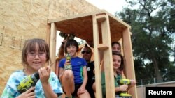 Tiny house builder Elvis Summers (middle) stands inside the shell of a tiny house he is building for a homeless veteran with some of the children helping him, in Santa Clarita, California, Aug. 2, 2017.
