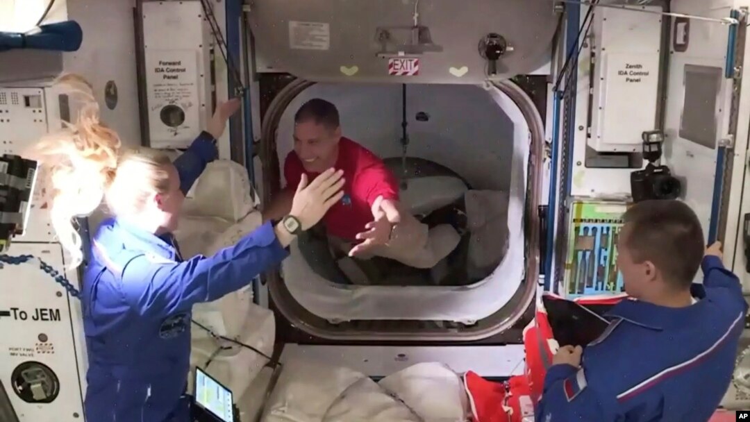 Astronaut Mike Hopkins (tengah), disambut oleh astronaut Kate Rubins (kiri) saat ia memasuki Stasiun Luar Angkasa Internasional (ISS) dari ruang depan antara kapsul SpaceX Dragon dan ISS, Selasa pagi, 17 November 2020. (NASA TV via AP)