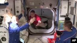 Astronaut Mike Hopkins (tengah), disambut oleh astronaut Kate Rubins (kiri) saat ia memasuki Stasiun Luar Angkasa Internasional (ISS) dari ruang depan antara kapsul SpaceX Dragon dan ISS, Selasa pagi, 17 November 2020. (NASA TV via AP)