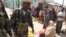 Women sell fruit at a market in Balad, Somalia on July 3, 2012, as soldiers stand guard. (VOA/M. Yusuf)