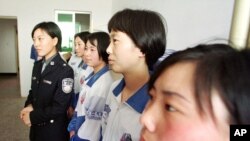 A female police officer is seen standing with women in a re-education camp in northeast China in this May 22, 2001, file photo.