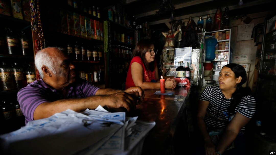 Trabajadores conversan cerca de una vela en un establecimiento durante un apagón en Caracas el 30 de agosto de 2024.