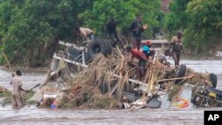 In this image made from video, people stand on an overturned vehicle swept by flooding waters in Chikwawa, Malawi, Jan. 25, 2022.