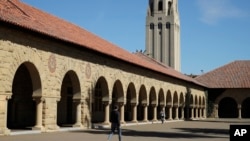 FILE- In this March 14, 2019, file photo, people walk on the Stanford University campus beneath Hoover Tower in Stanford, Calif.