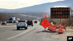 FILE - Construction signs warn drivers of lane closures along US Route 550 as crews prepare to begin work on the highway in Bernalillo, N.M., Feb. 19, 2015.