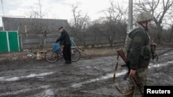 FILE - A man pushes a bicycle past a Ukrainian soldier, who stands guard in a street March 3, 2021, in the town of Novhorodske, Donetsk region, Ukraine, where fighting between government forces and Russia-backed separatists continues. 