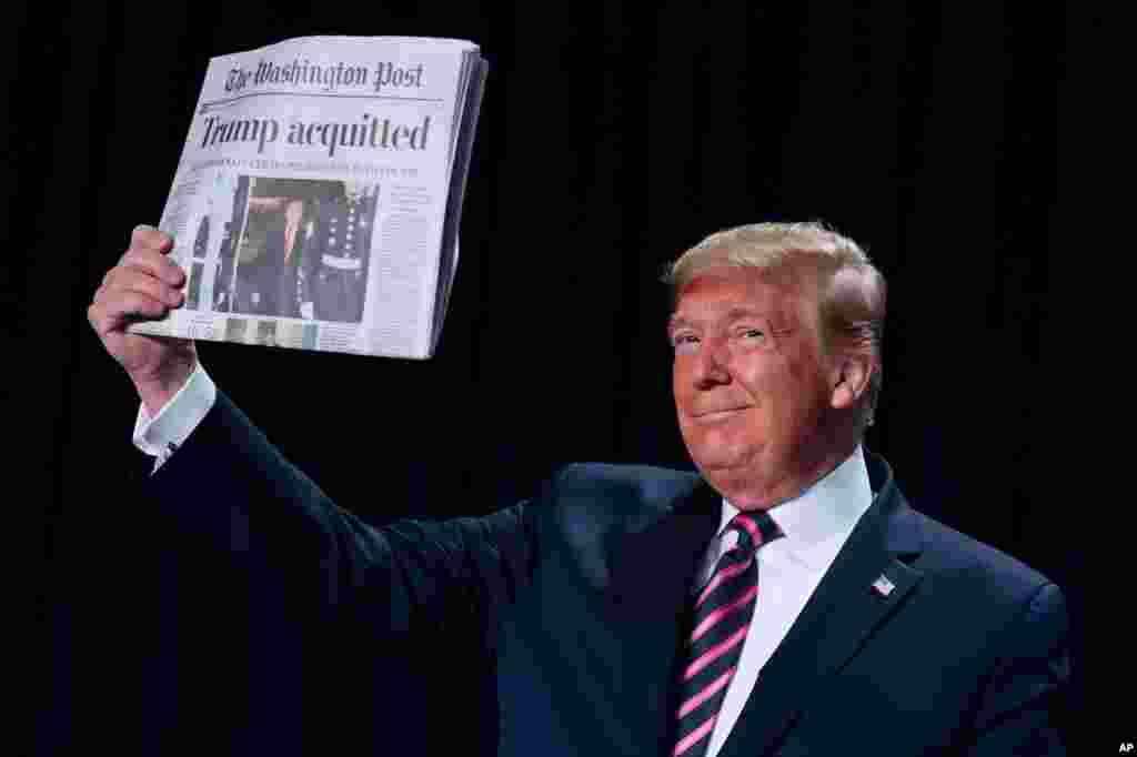 President Donald Trump holds up a newspaper with the headline that reads &quot;Trump acquitted&quot; during the 68th annual National Prayer Breakfast, at the Washington Hilton in Washington.