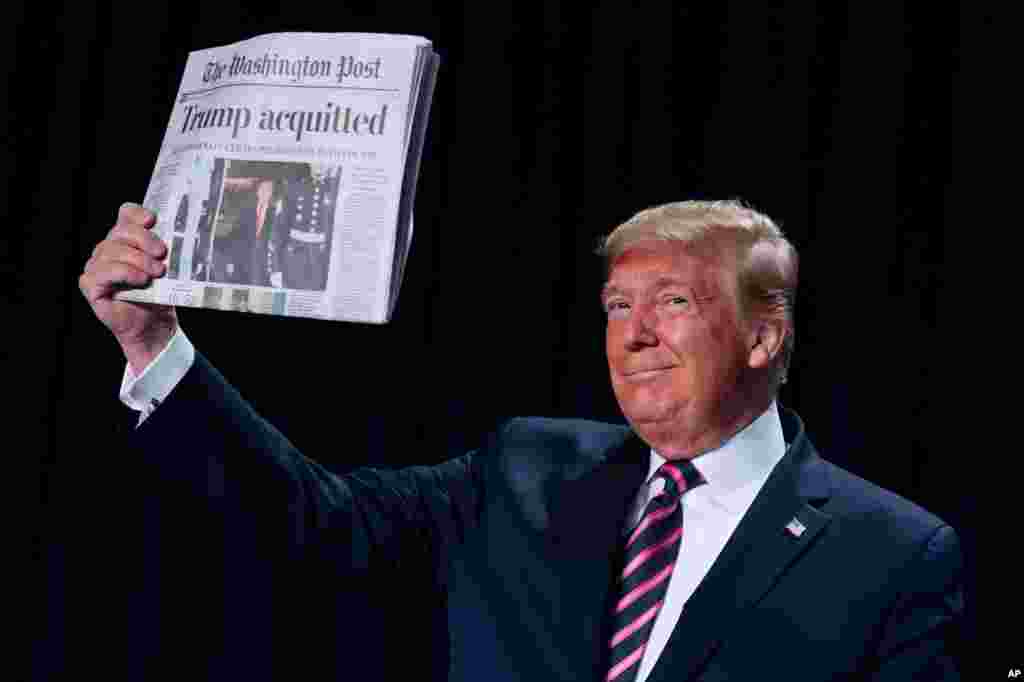 President Donald Trump holds up a newspaper with the headline that reads "Trump acquitted" during the 68th annual National Prayer Breakfast, at the Washington Hilton in Washington.