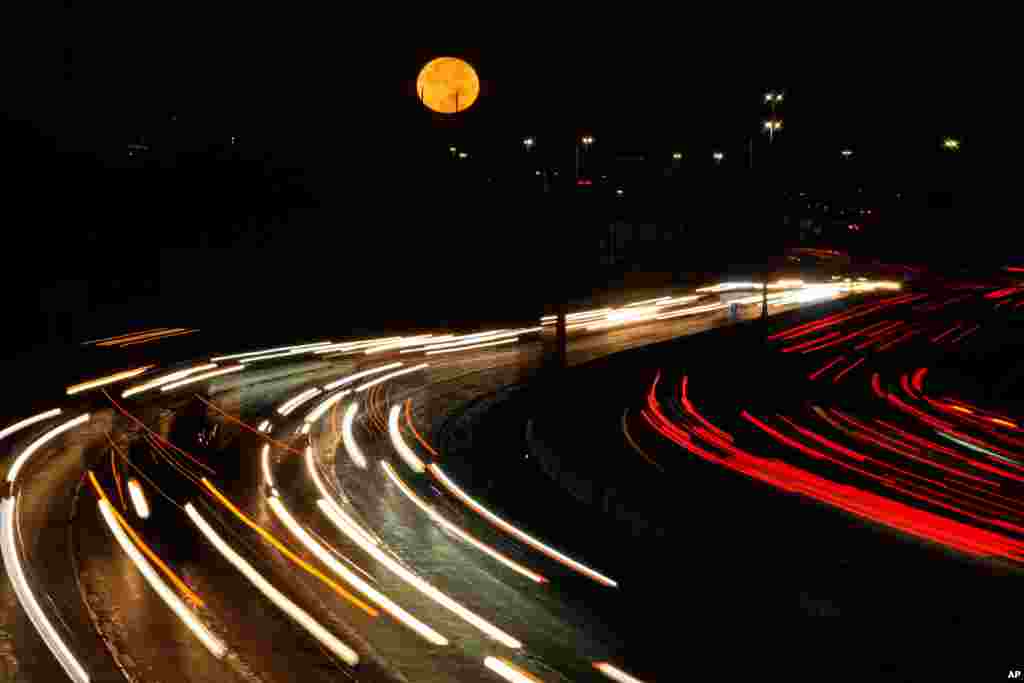 The full moon sets as morning traffic travels on a freeway in Leawood, Kansas.