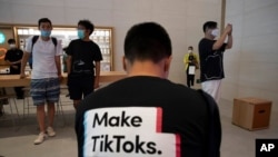 Një burrë që mban veshur një bluzë ku reklamohet platforma TikTok, qëndron i ulur në dyqanin e kompanisë Apple në Pekin.
