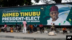 People sit under a billboard with a congratulatory message of the President-Elect Bola Ahmed Tinubu of the All Progressives Congress in Lagos, Nigeria, March 5, 2023.