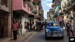 ARCHIVO - La gente camina bajo un cartel que anuncia una tienda de comestibles privada, a la izquierda, en La Habana, el 11 de noviembre de 2023. 