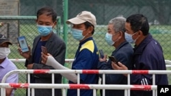 Residents wearing face masks to help curb the spread of the coronavirus look at their smartphones showing health code as they line up to receive the Sinopharm COVID-19 vaccine at a vaccination center in Central Business District in Beijing on…