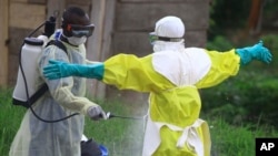 In this photo taken Sept. 9, 2018, a health worker sprays disinfectant on his colleague after working at an Ebola treatment center in Beni, Eastern Congo.