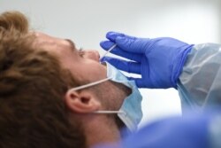 A healthcare worker uses a swab to collect a sample from a man testing for the novel coronavirus COVID-19 at a primary health care center in Barcelona on Aug. 3, 2020.