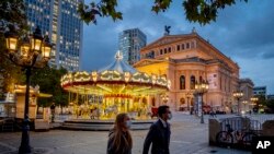 People wearing face masks walk past a carousel and the Old Opera in Frankfurt, Germany, Oct. 28, 2020. 