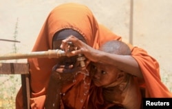 FILE - Fadumo Isaq Abdi, an internally displaced Somali woman, holds her child Maria Mohamed Ali as they drink water outside the feeding center, a new site for IDPs, in Barwaaqo, near Baidoa, Somalia, Feb. 21, 2023.