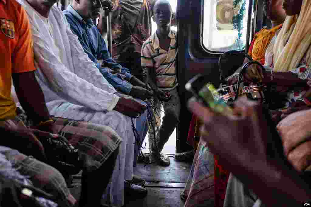 Among passengers on their mobile phones and clutching prayer beads, an apprentice stands at the back holding money he has collected as fares. (R. Shryock/VOA)