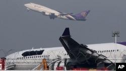 FILE - A Thai Airways passenger plane takes off over a damaged Thai Airways Airbus A330-300 that skidded off the runway while landing at Suvarnabhumi International Airport in Bangkok, Thailand, Sept. 9, 2013.