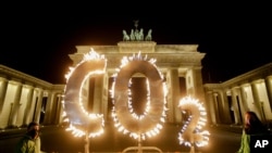 FILE - Activists of the environment organization Greenpeace protest with CO2 letters illuminated with flames in front of the Brandenburg Gate against the climate change in Berlin, Germany, May 6, 2021. 