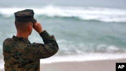 FILE - A U.S. Marine Corps officer uses binoculars to search for debris of two helicopters missing off the coast of Hawaii, in Haliewa Beach Park, Hawaii, Jan. 15, 2016.