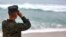 FILE - A U.S. Marine Corps officer uses binoculars to search for debris of two helicopters missing off the coast of Hawaii, in Haliewa Beach Park, Hawaii, Jan. 15, 2016.