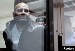 FILE - Sergei Khadzhikurbanov is escorted into a glass-walled cage before a court hearing in Moscow, June 3, 2013. Convicted in the assassination of journalist Anna Politkovskaya, he has been pardoned after fighting in the war in Ukraine.