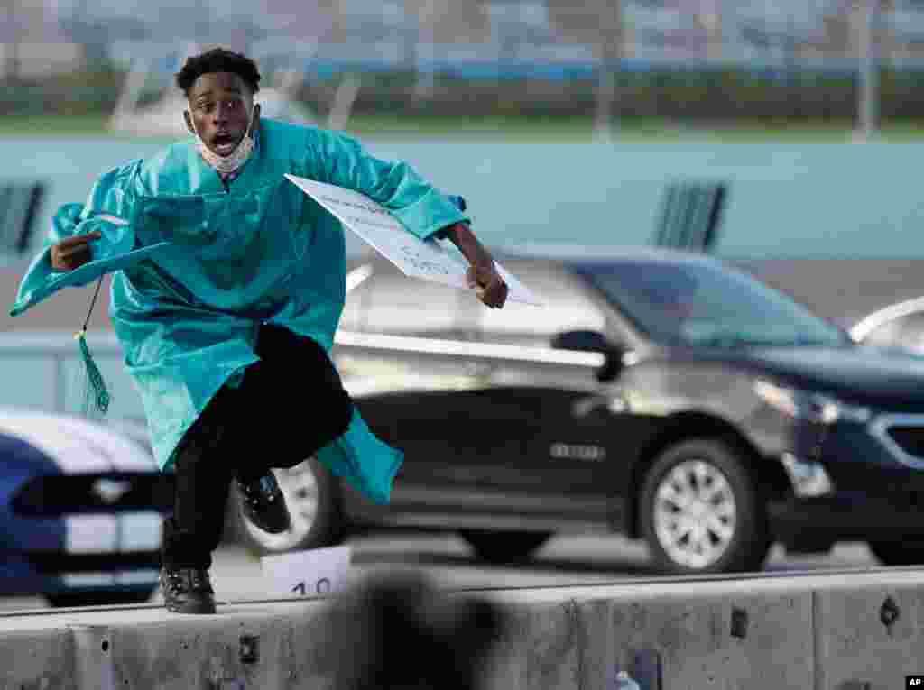 Richardson Fremond leaps over a wall as he runs to collect an award during a graduation ceremony for the senior class of Chambers High School at Homestead-Miami Speedway, in Homestead, Fla., June 23, 2020.